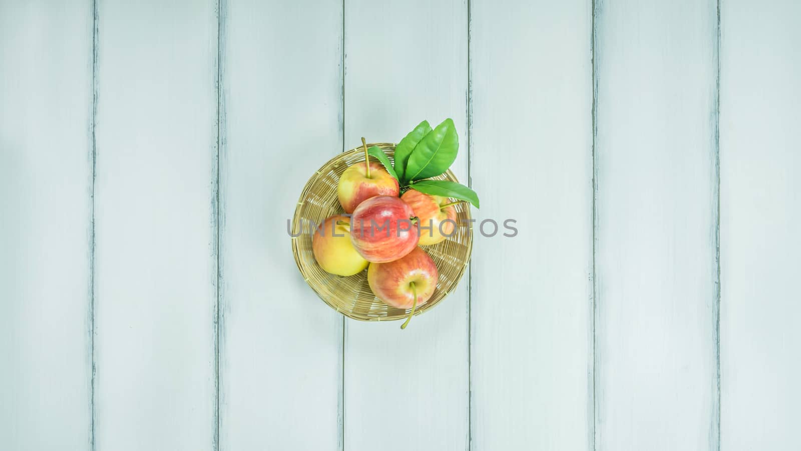 Top view red and yellow apple with leaves and  bamboo basket on  white wooden background with free space for text