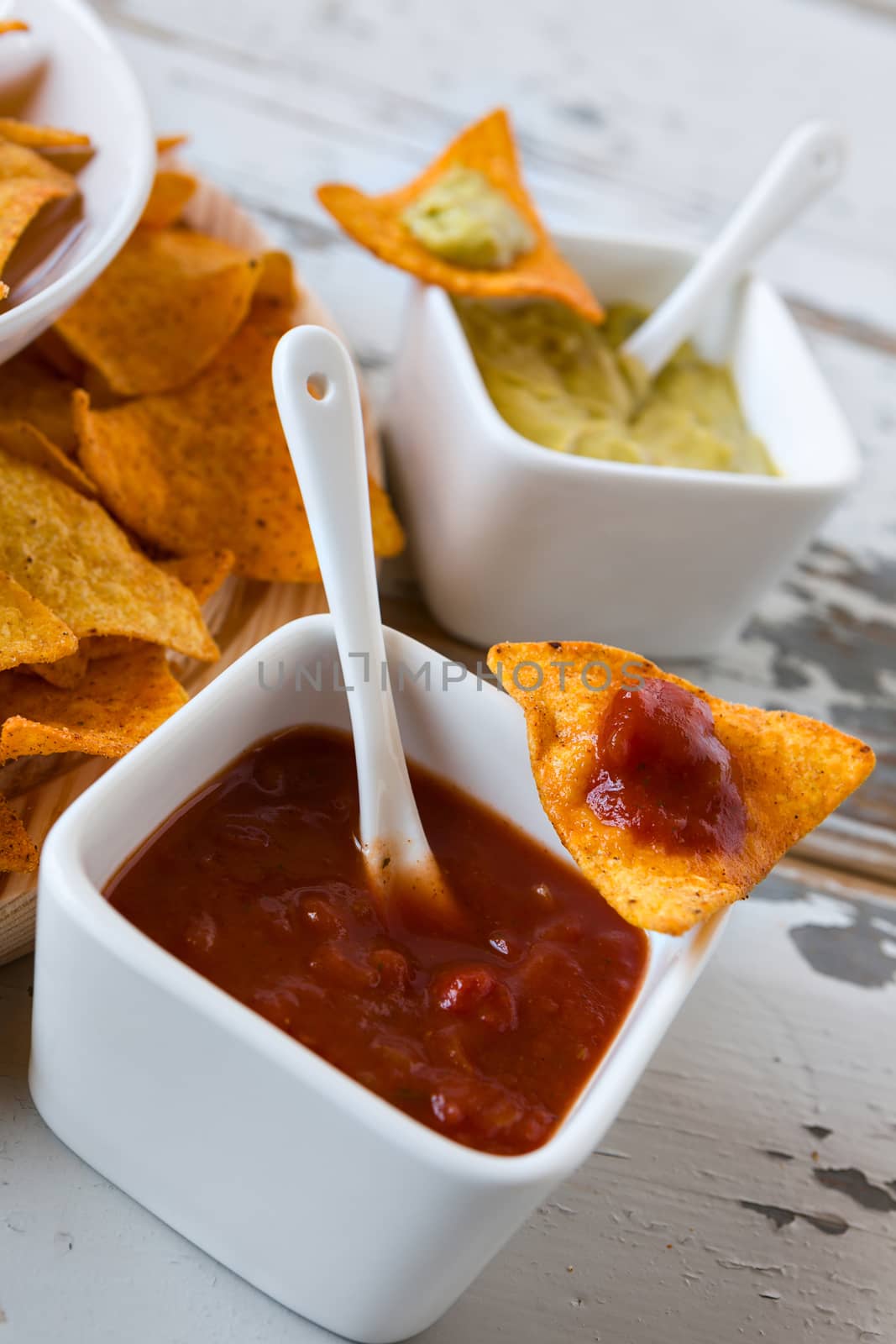Chili sauce and nachos chips with guacamole sauce on background over an old wooden table