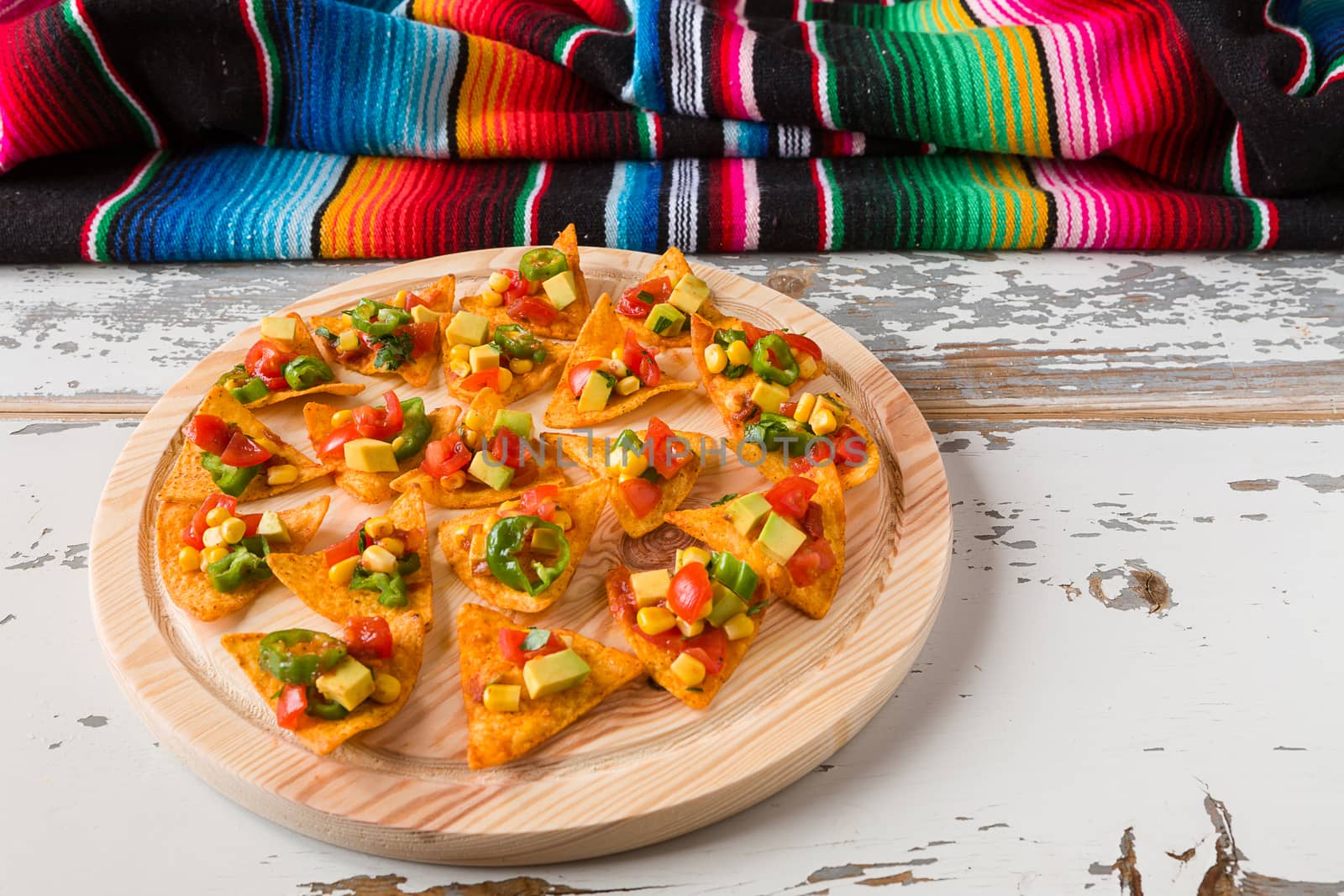 Nachos chips with vegetables on a chopping board and a poncho over an old wooden table