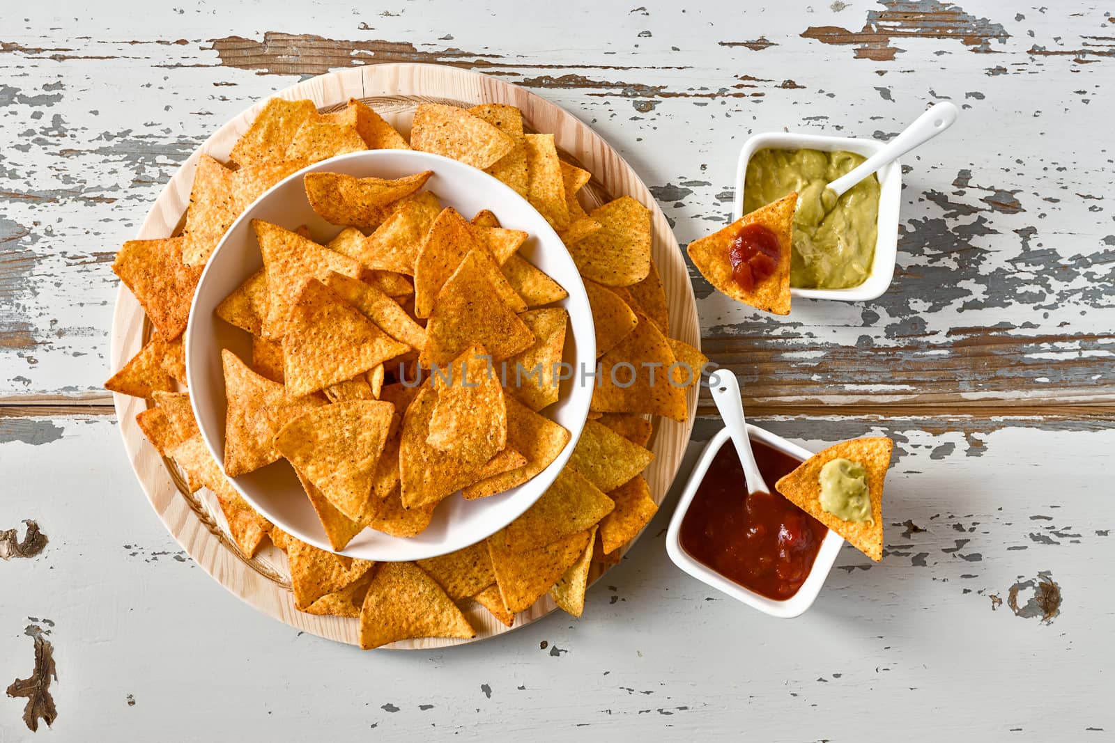 Nachos in a white bowl and sauces seen from above over a wood background