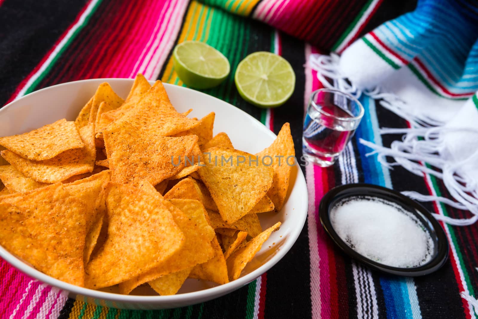 Nachos chips in a bowl tequila lime and salt over a colored poncho