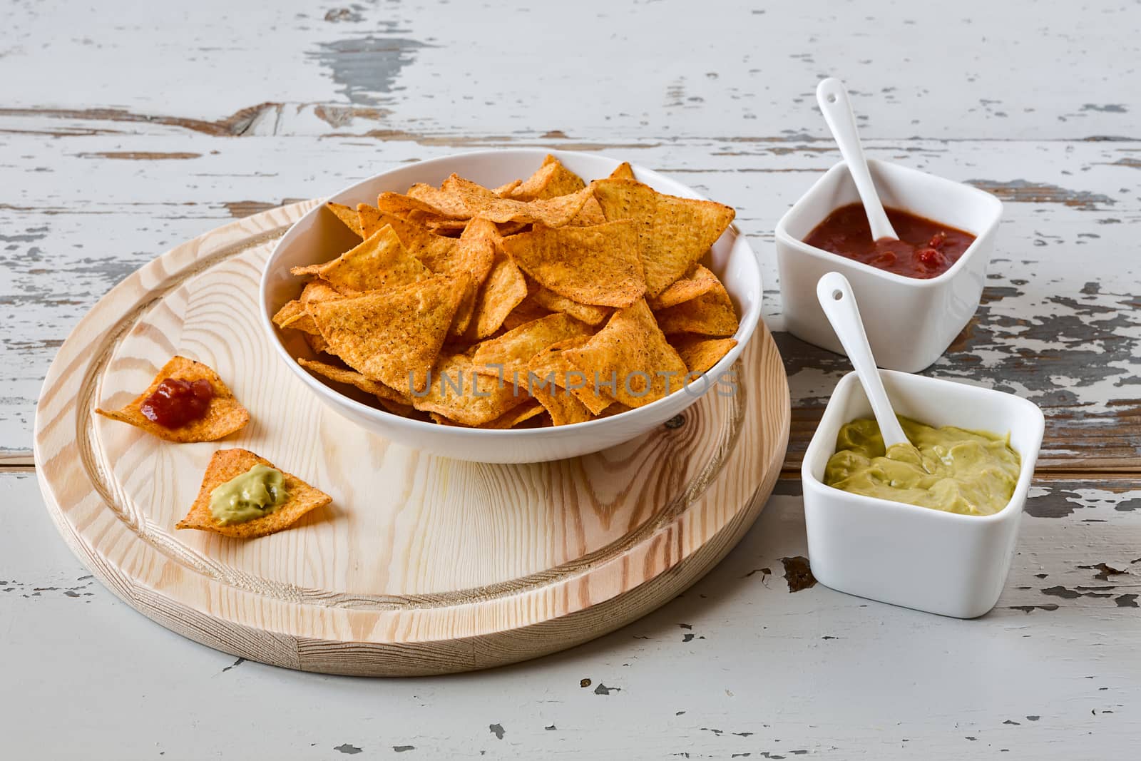 Nachos chips with sauce on a chopping board on a wood background