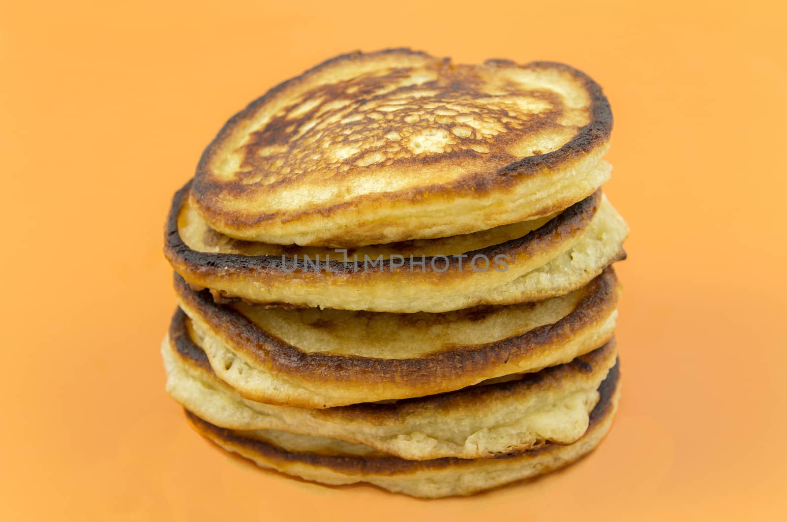 A pile of delicious fresh oil-bearing thick pancakes on a yellow background