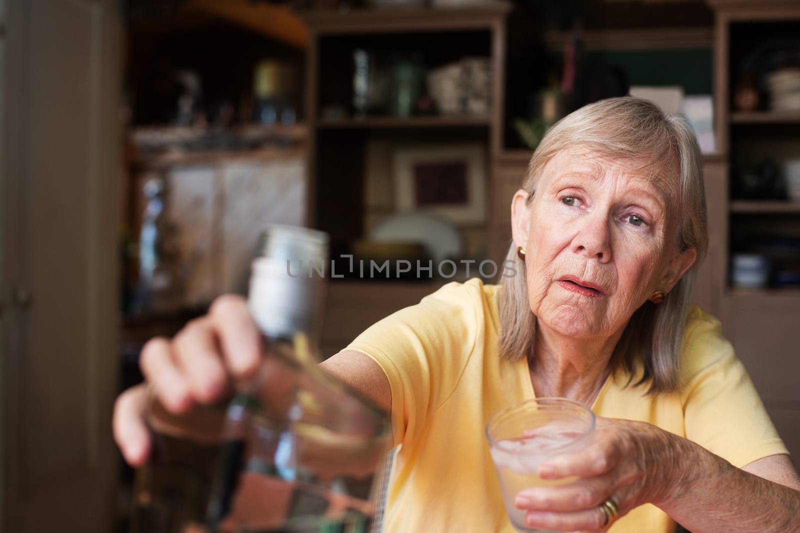 Lonely senior adult female reaching for a bottle of liquor while holding a glass