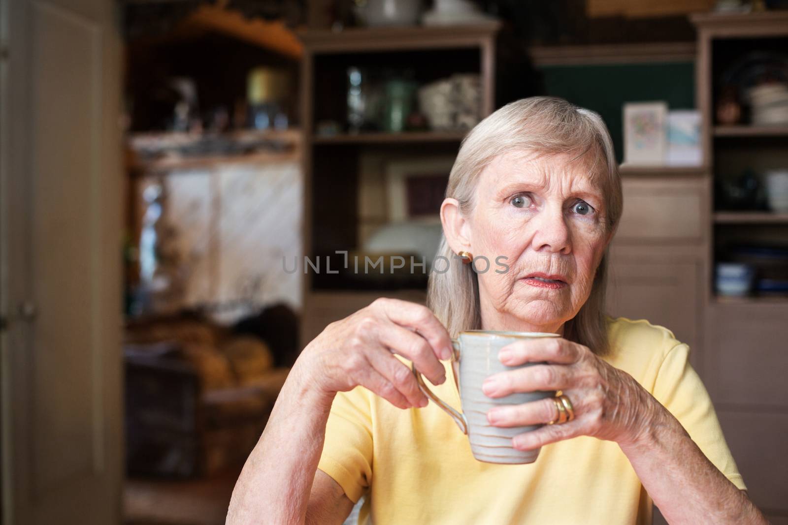 Worried senior woman holding coffee cup by Creatista