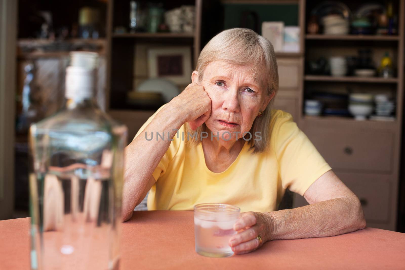 Solitary woman in yellow shirt with hand on face while holding glass of vodka