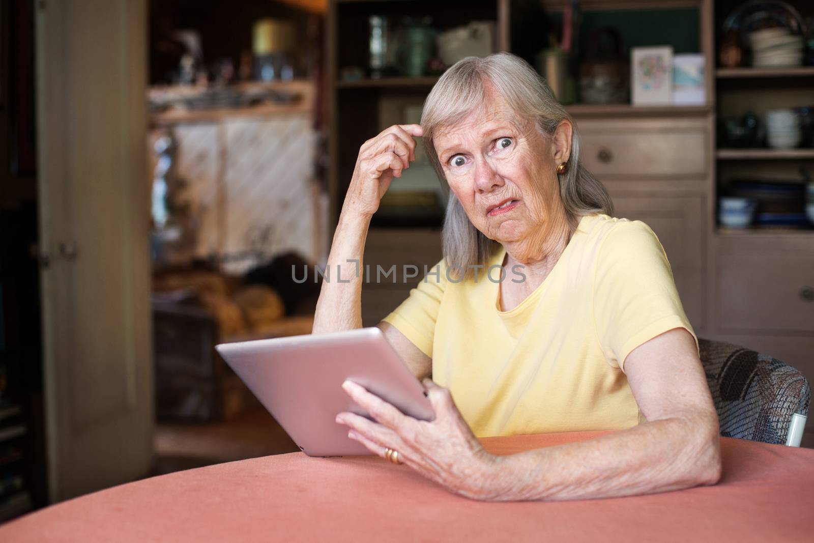 Single older female adult with confused expression holding tablet computer
