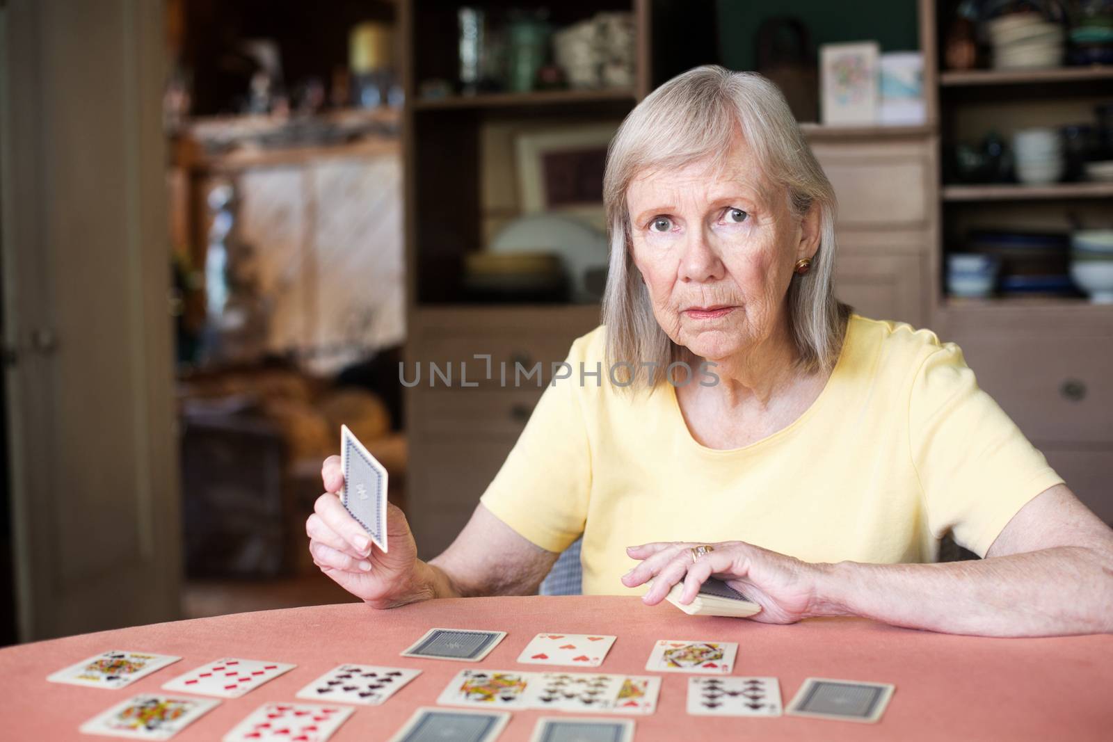 Woman in yellow shirt with serious expression and playing cards spread out