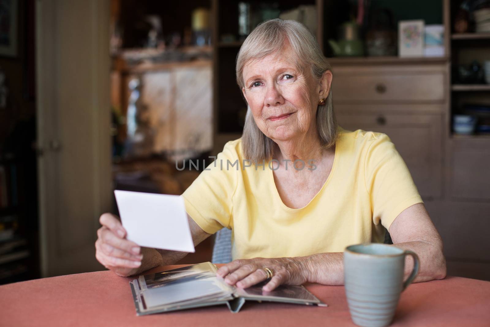 Proud senior woman hold photo from picture album while seated near coffee cup