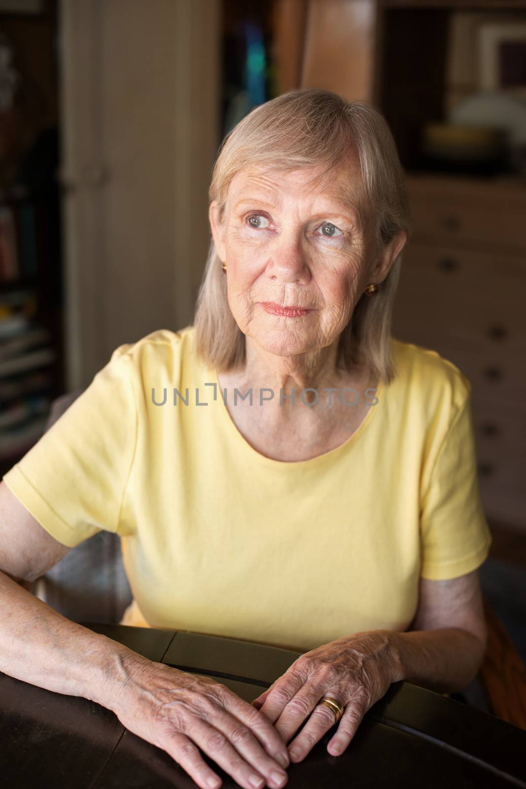 Serious senior woman seated at table by Creatista