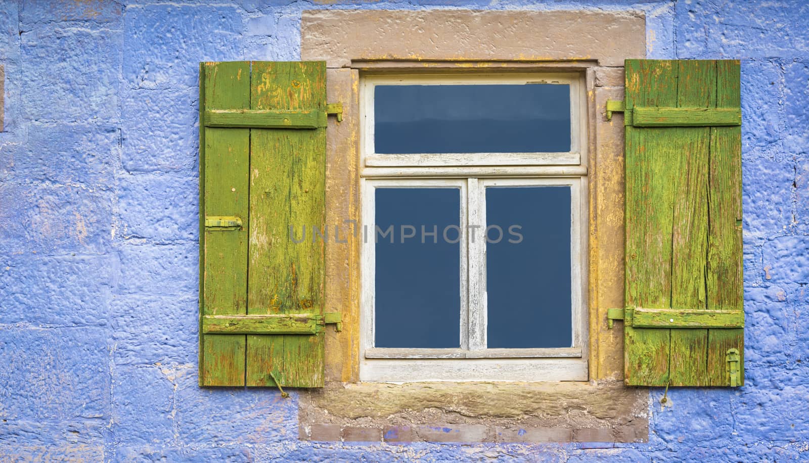 Aged wooden window and green shutters from an old german house with blueish painted wall stone