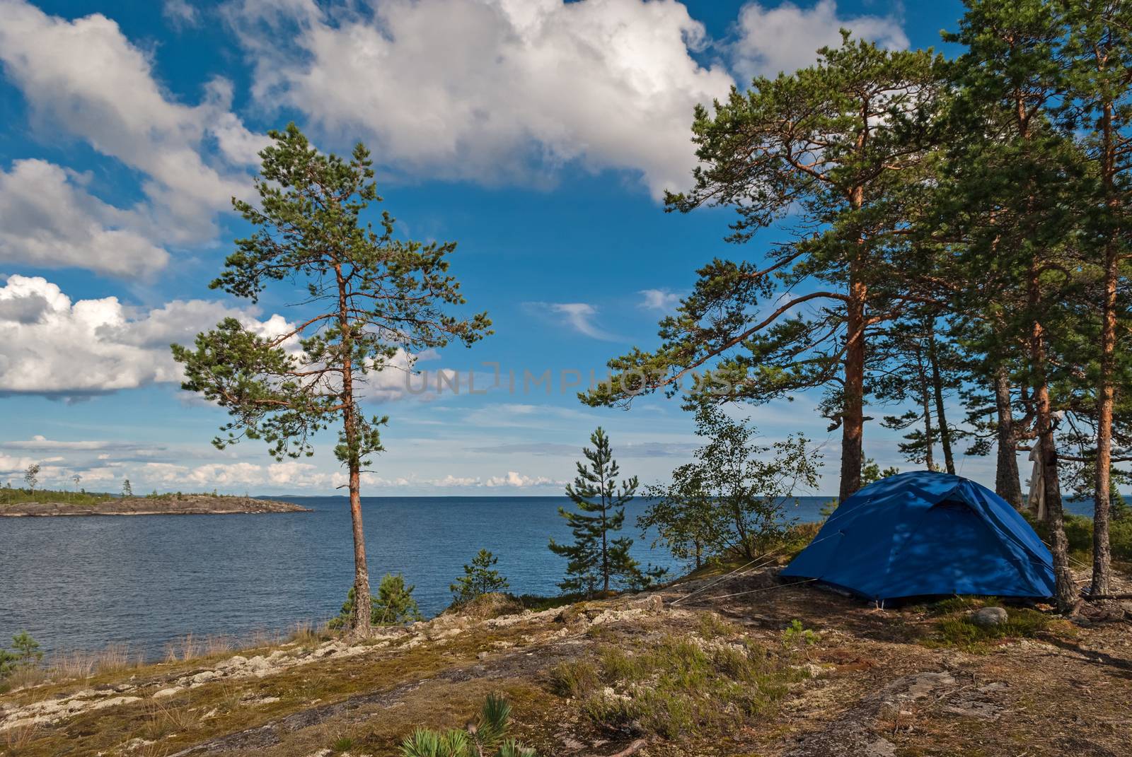 Blue tourist tent on the rocky shore of Lake Ladoga on the background of blue sky with white clouds in Karelia.