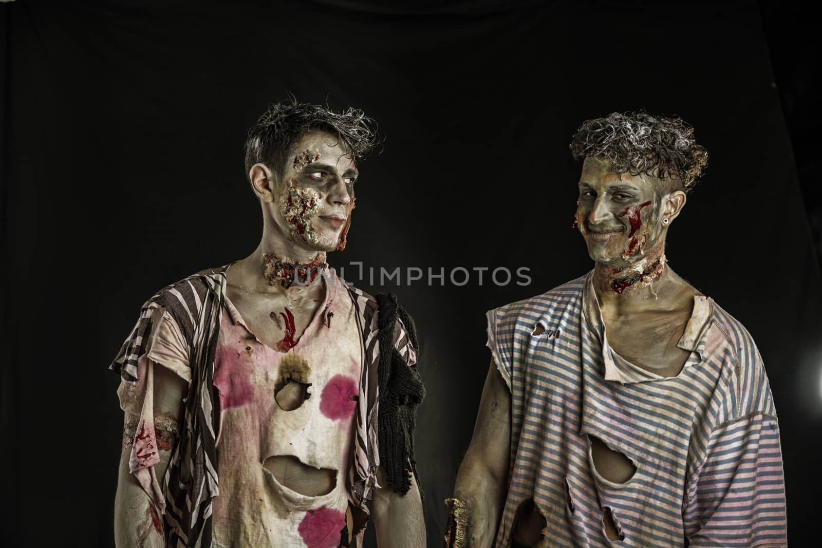 Two male zombies standing on black background, looking at each other smiling