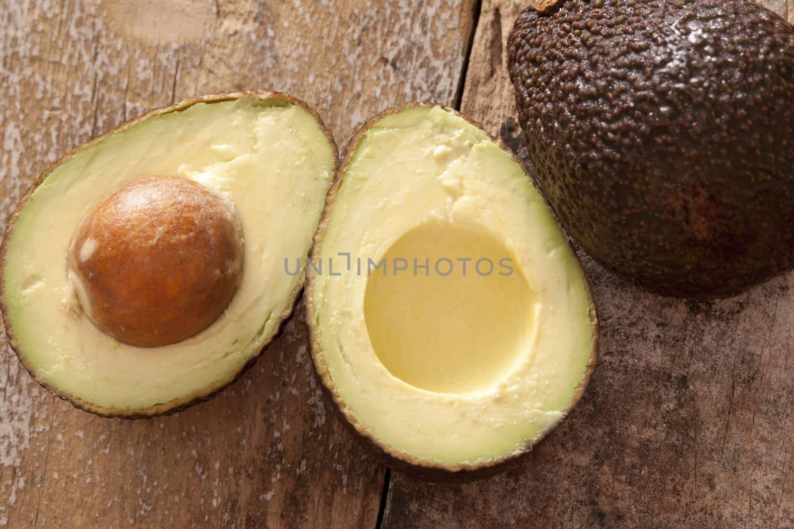 Halved healthy ripe tropical avocado pear with the pip or seed still in alongside a whole fruit on a wooden table in an overhead view