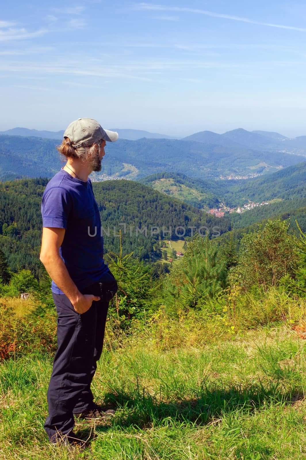 a bearded man, hiker with backpack, standing in the mountains and looks into the distance. Back view. Sunny day.