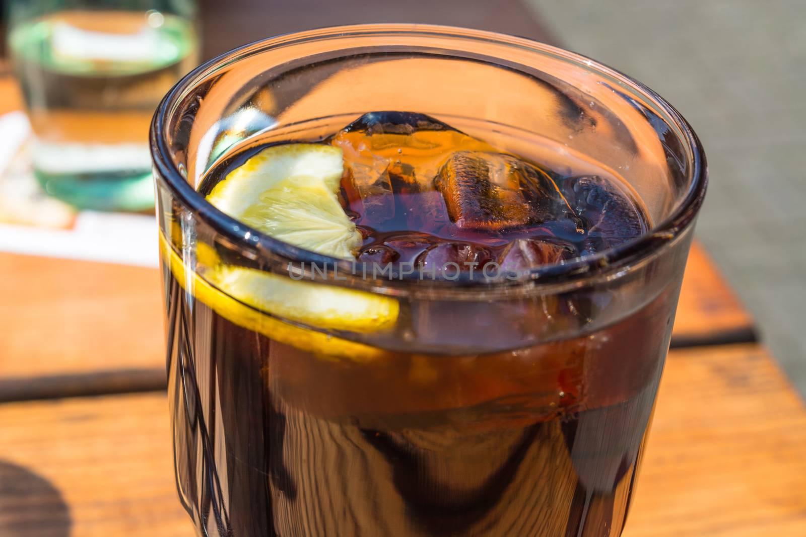 Detail, glass of cola with ice and lemon on a wooden table.