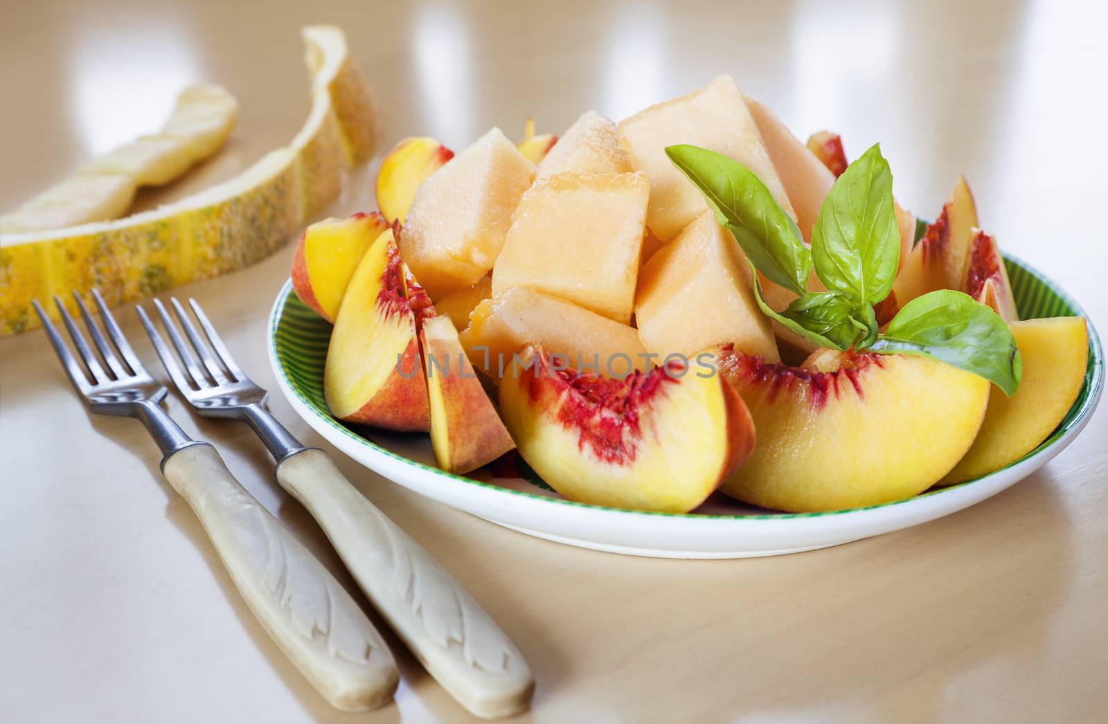 Plate with sliced fruits - peaches and melon with fresh basil and two forks
