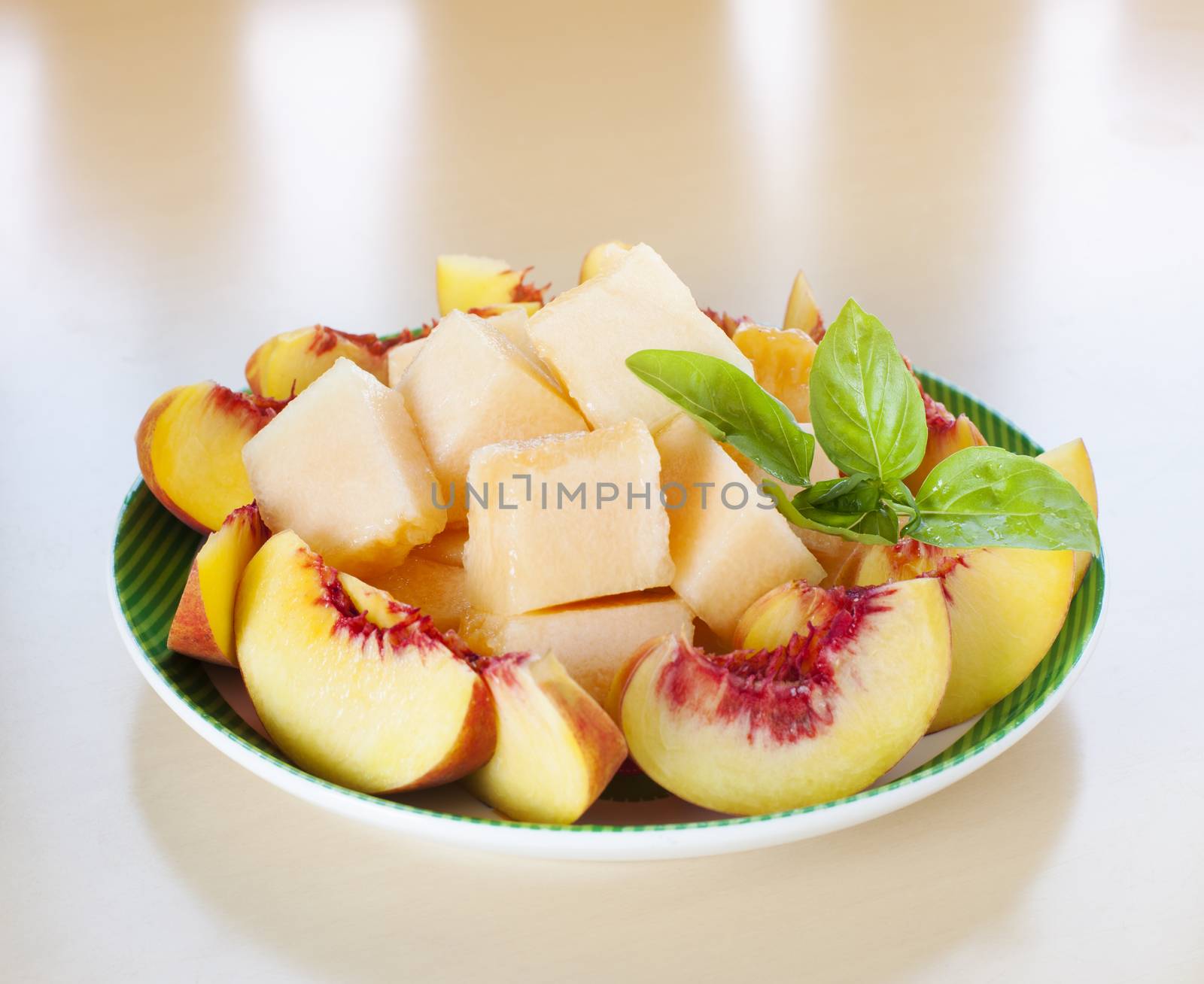 Plate with sliced fruits - peaches and melon with fresh basil.