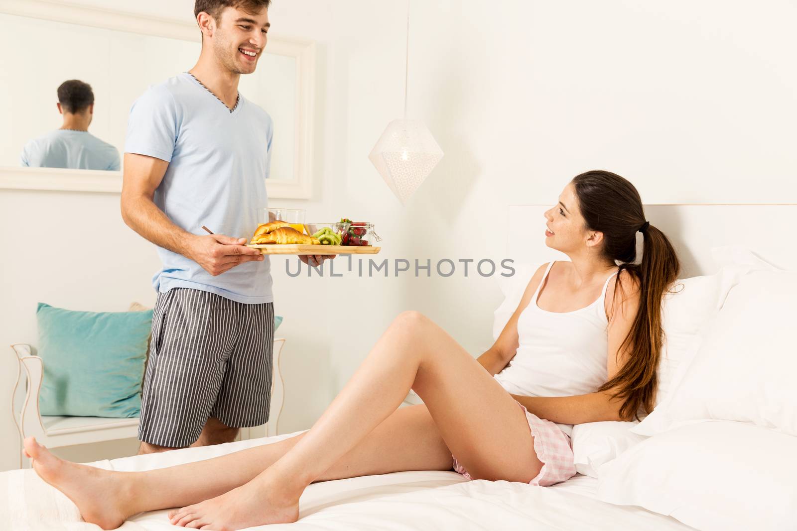 Couple on a hotel room, and the man serving breakfast on bed