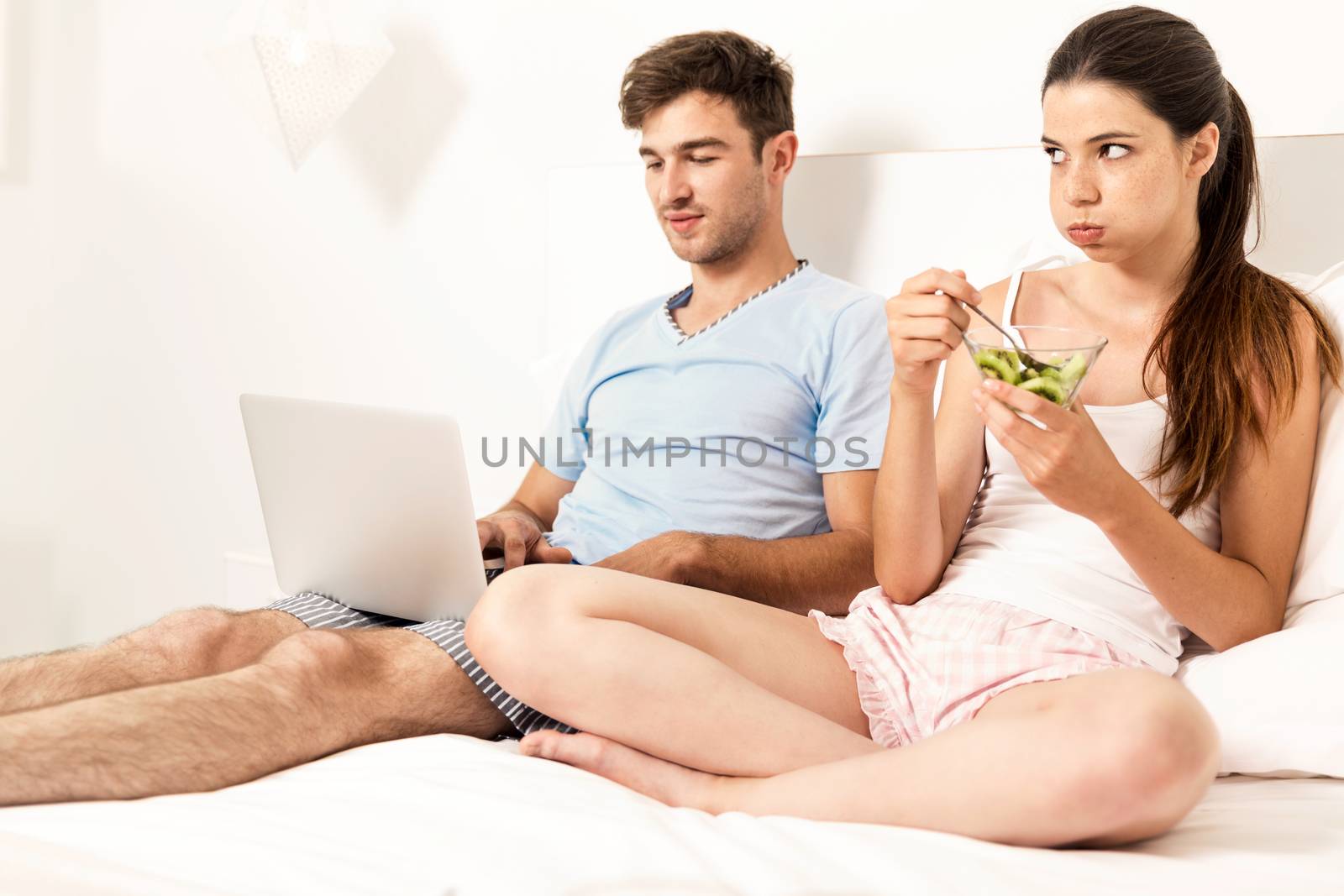 Addicted young man on bed with a laptop while the woman looks angry