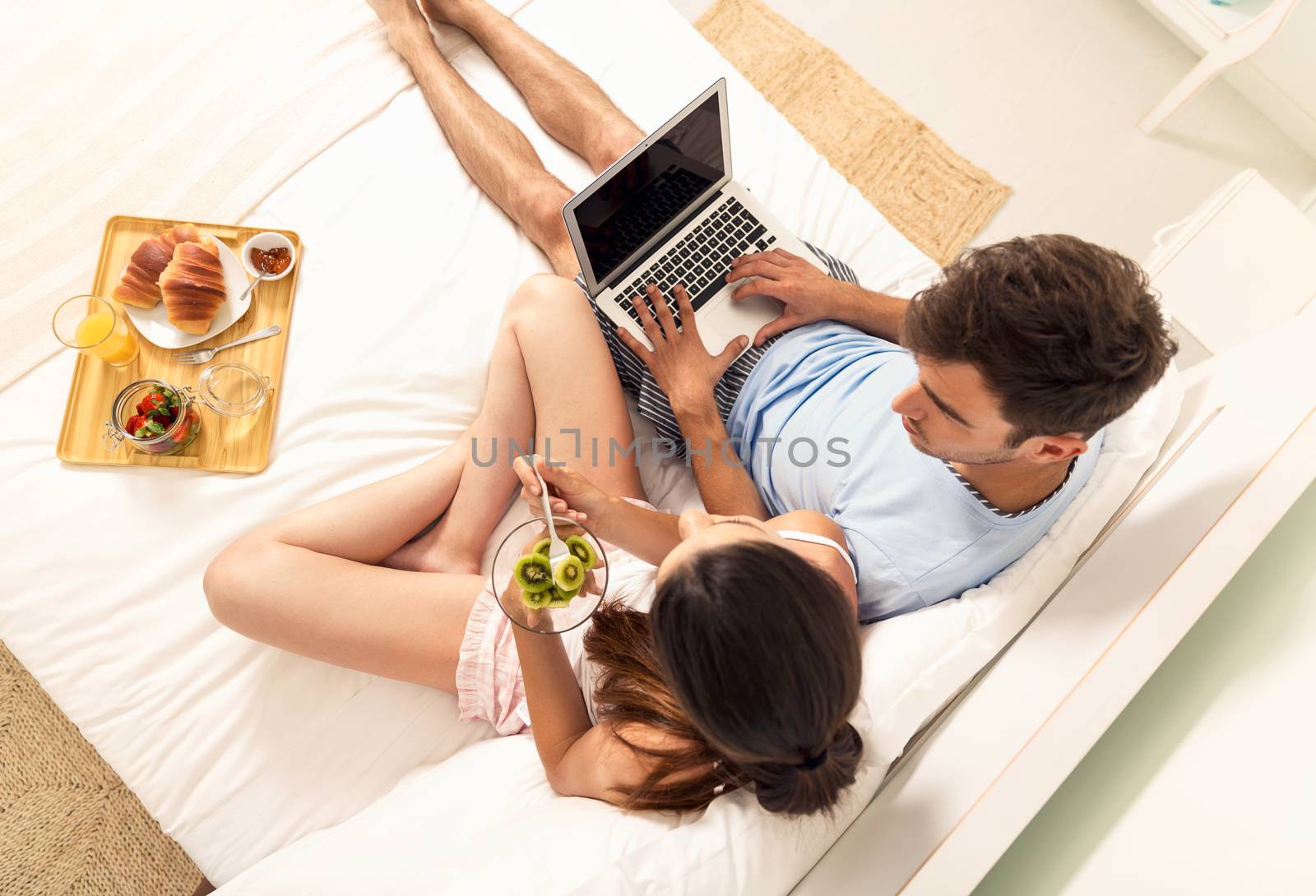 Young couple siting on bed working and eating breakfast