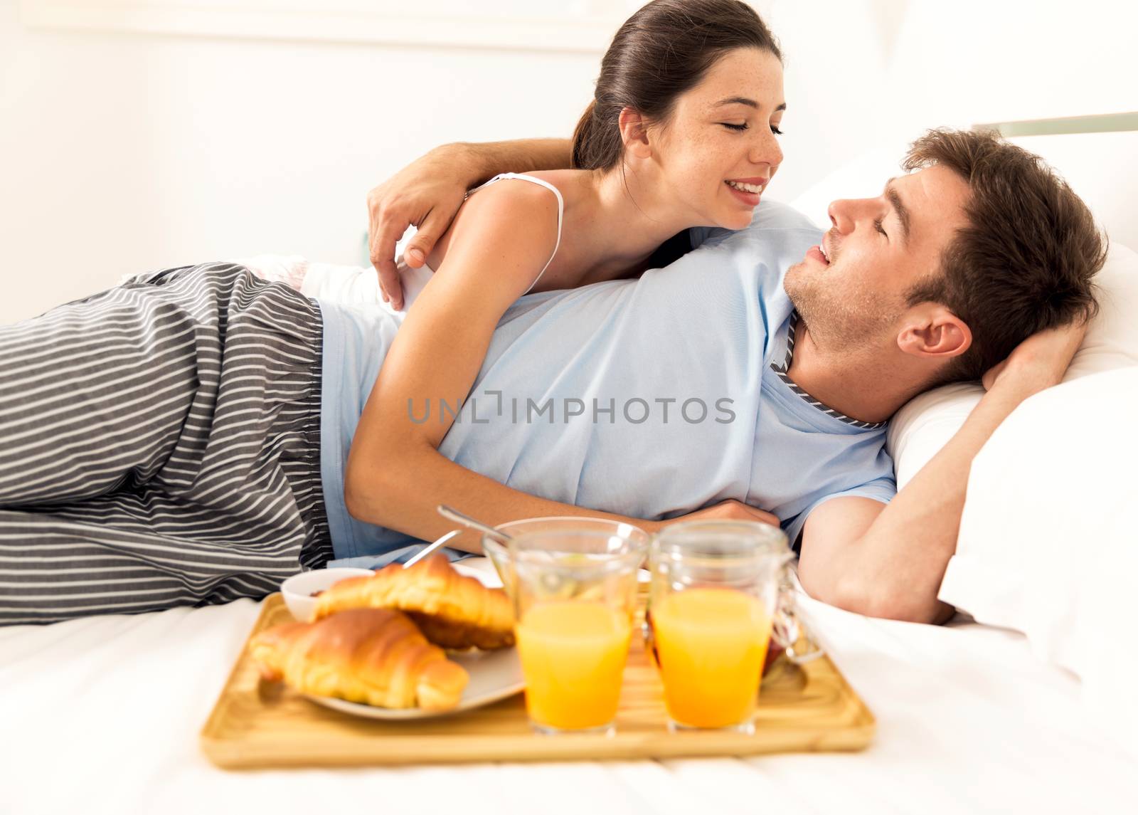 Young couple lying on the bed with breakfast on bed 