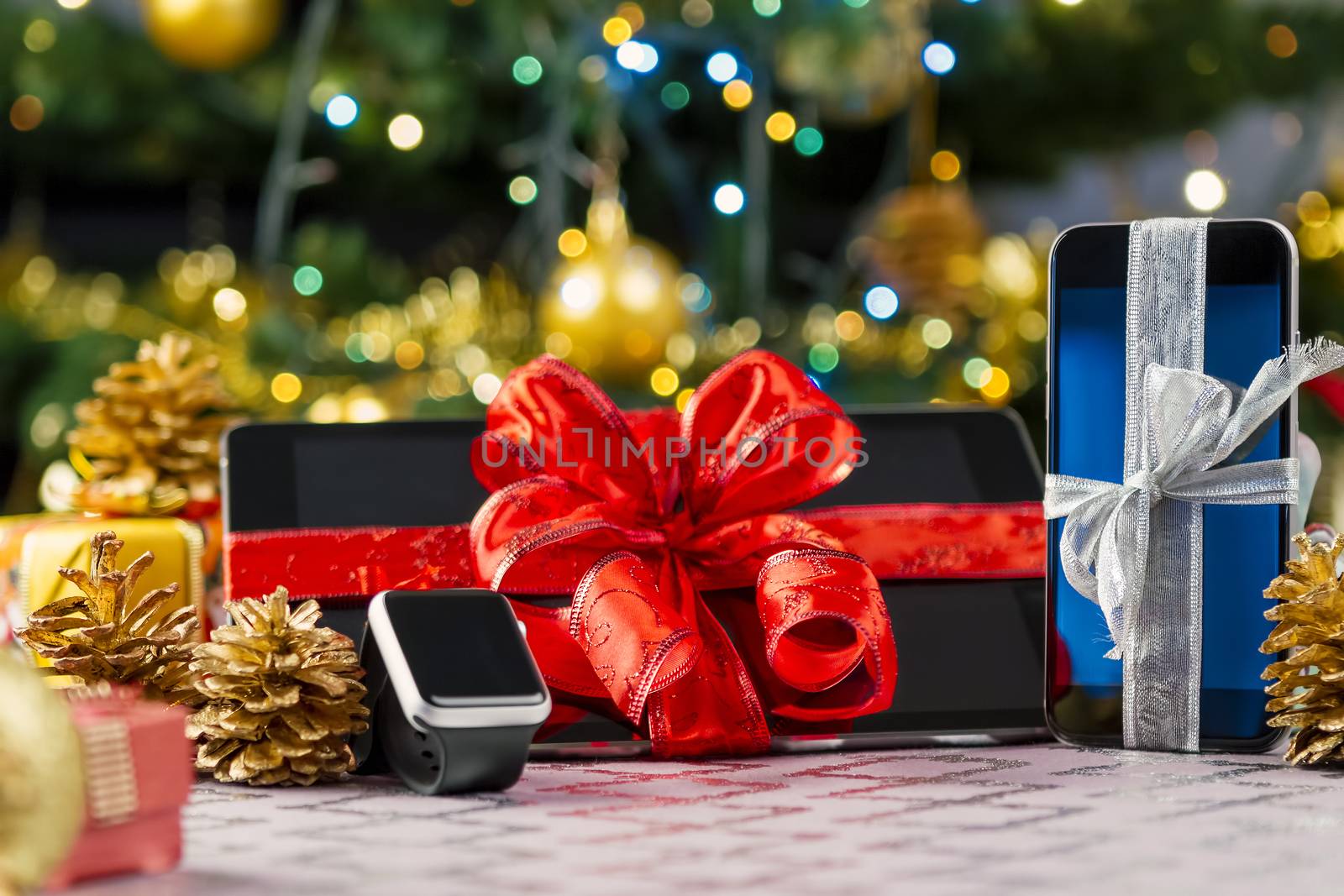 Tablet pc, smartphone and smartwatch with gifts and decorations in front of Christmas tree. Focus on smartphone.