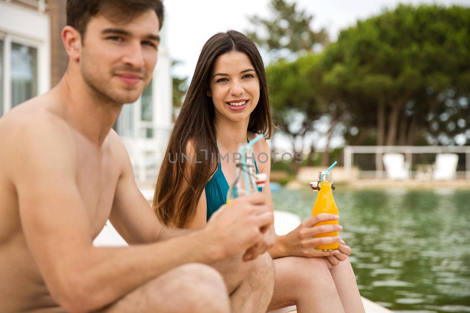 Young couple sitting by the pool and drinking natural juices