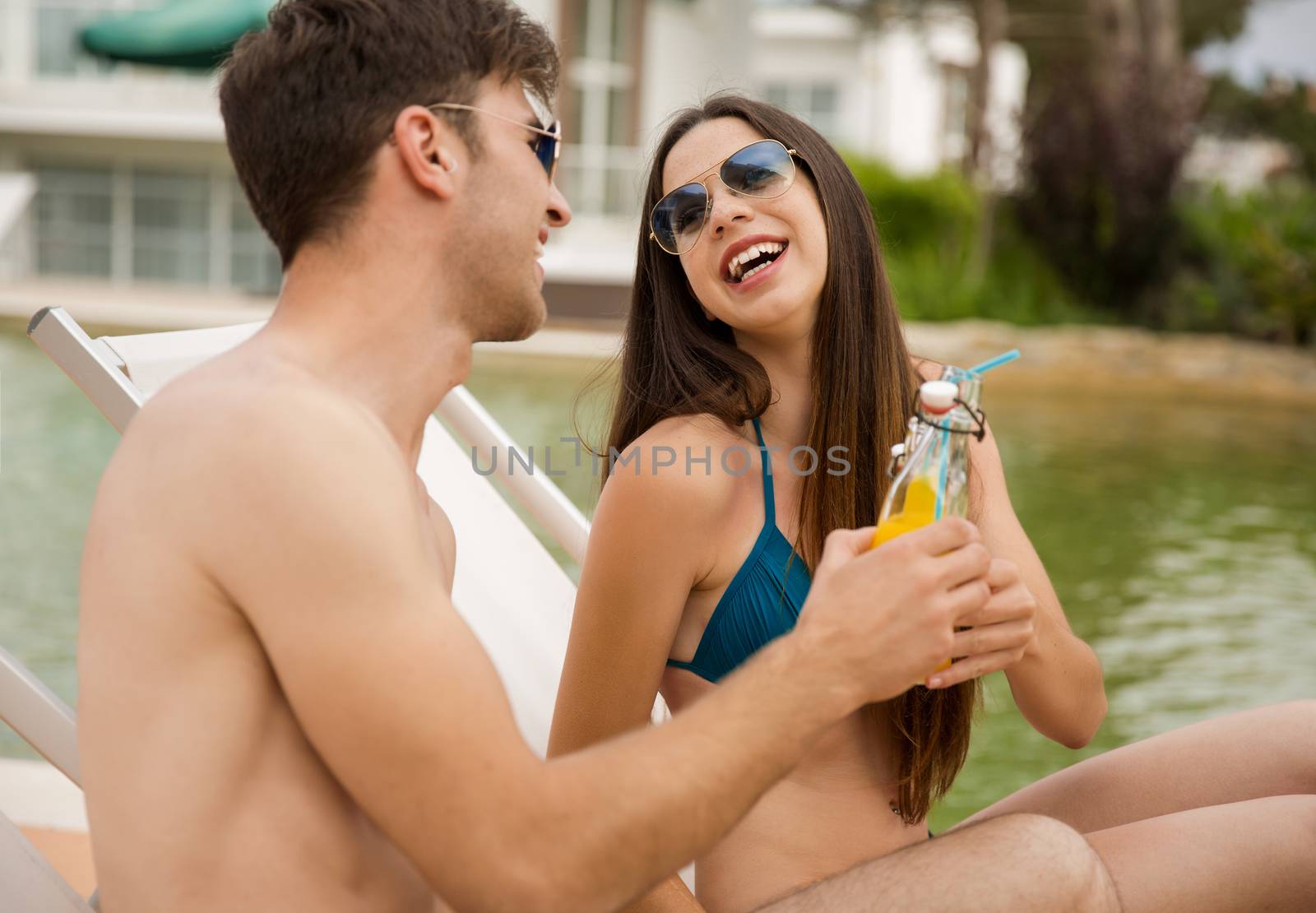 Young couple sitting by the pool and drinking natural juices