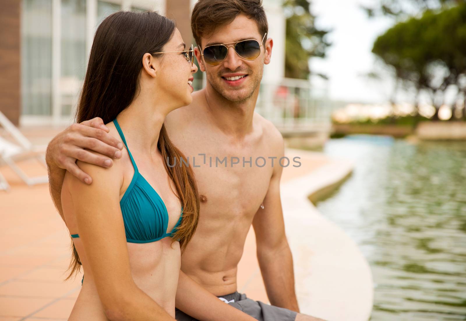 Young couple sitting by the pool and enjoying the vacations