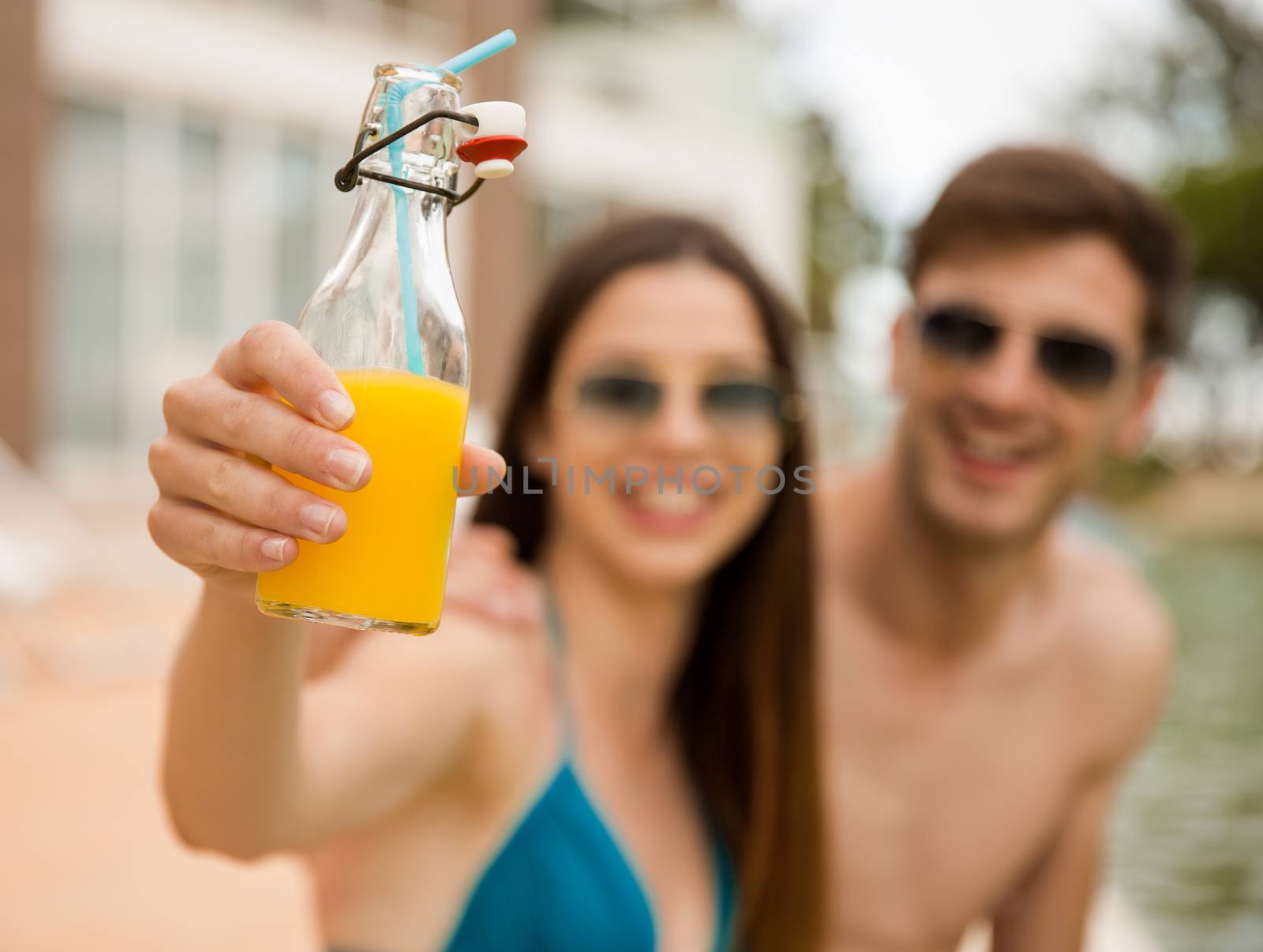 Young couple sitting by the pool and drinking natural juices