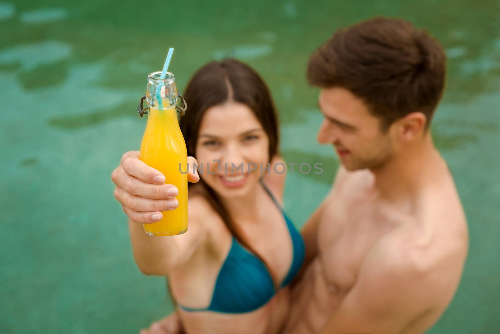 Young couple inside the pool and drinking natural juices