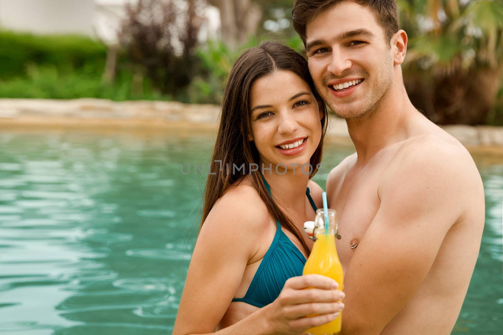 Young couple inside the pool and drinking natural juices