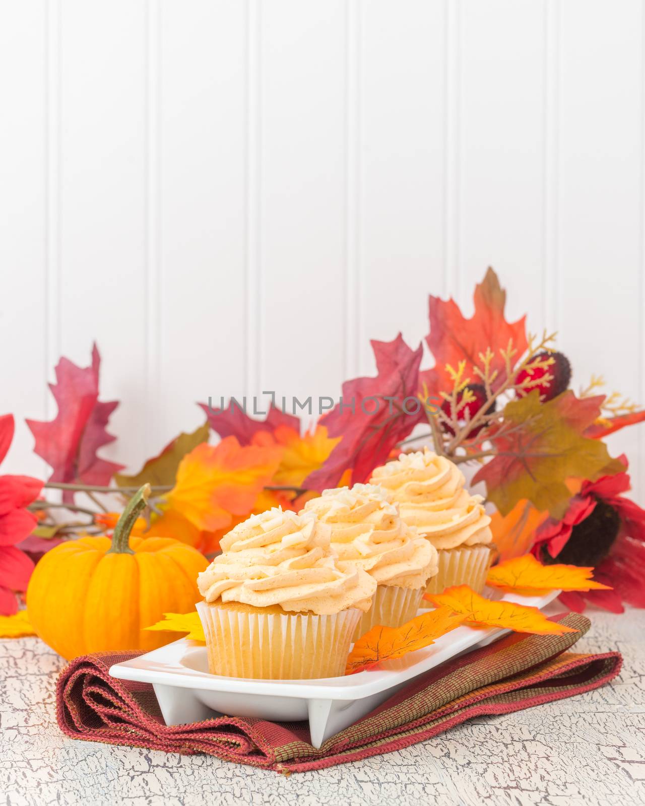 Three pumpkin spice cupcakes surrounded by beautiful fall foliage.