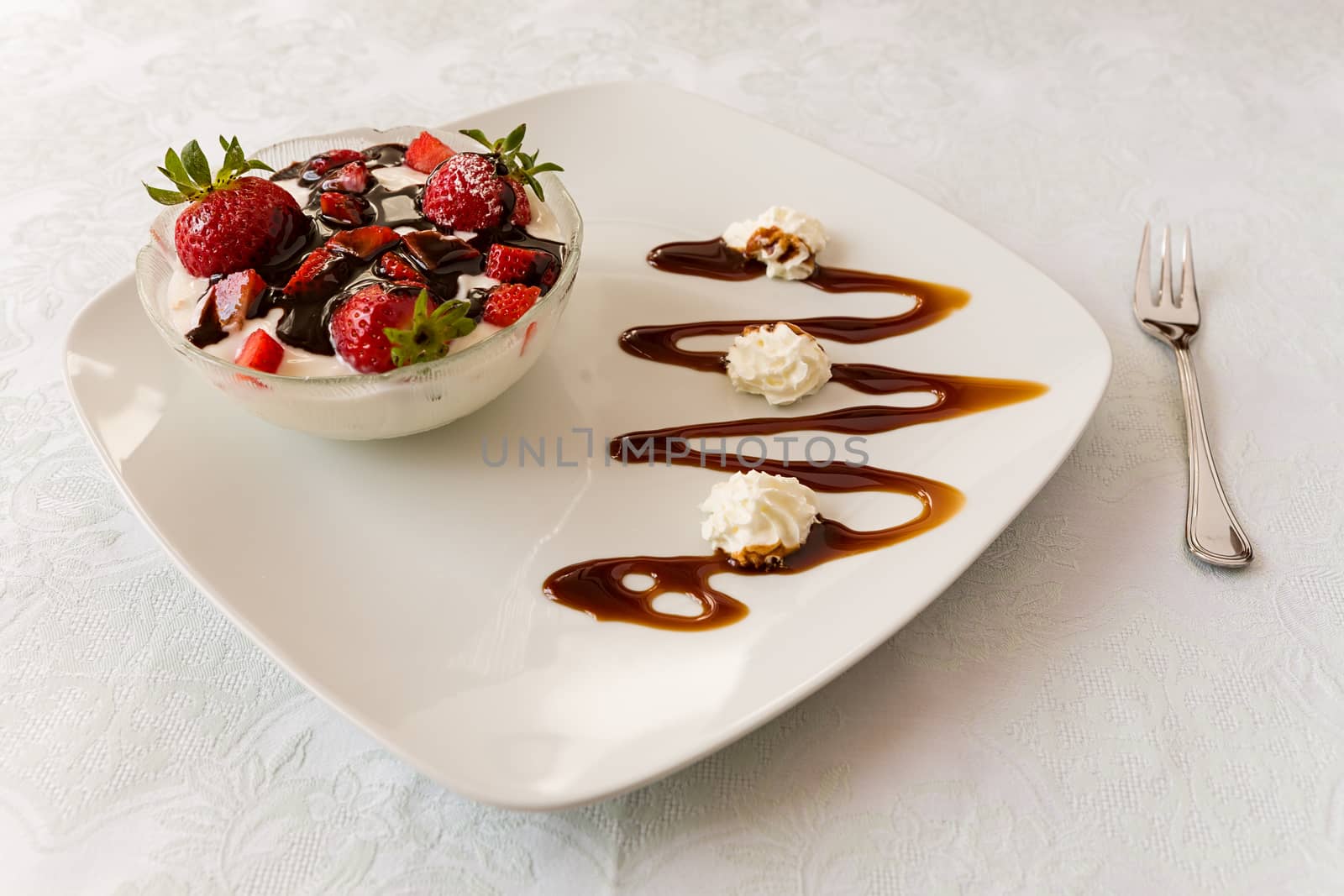 Dessert with strawberries and yogurt in a bowl over a square plate with decorations and cream