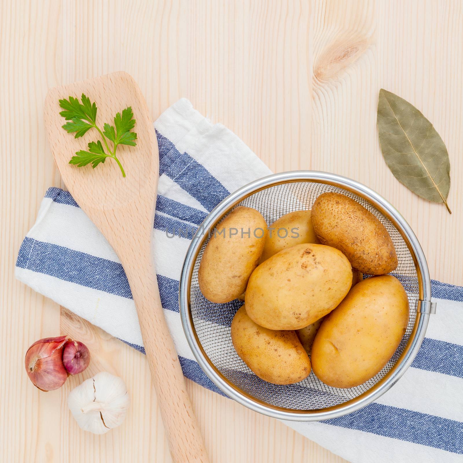 Fresh organic potatoes in basket with herbs garlic,shallot ,parsley and bay leaves on rustic wooden table. Preparation for cooking.