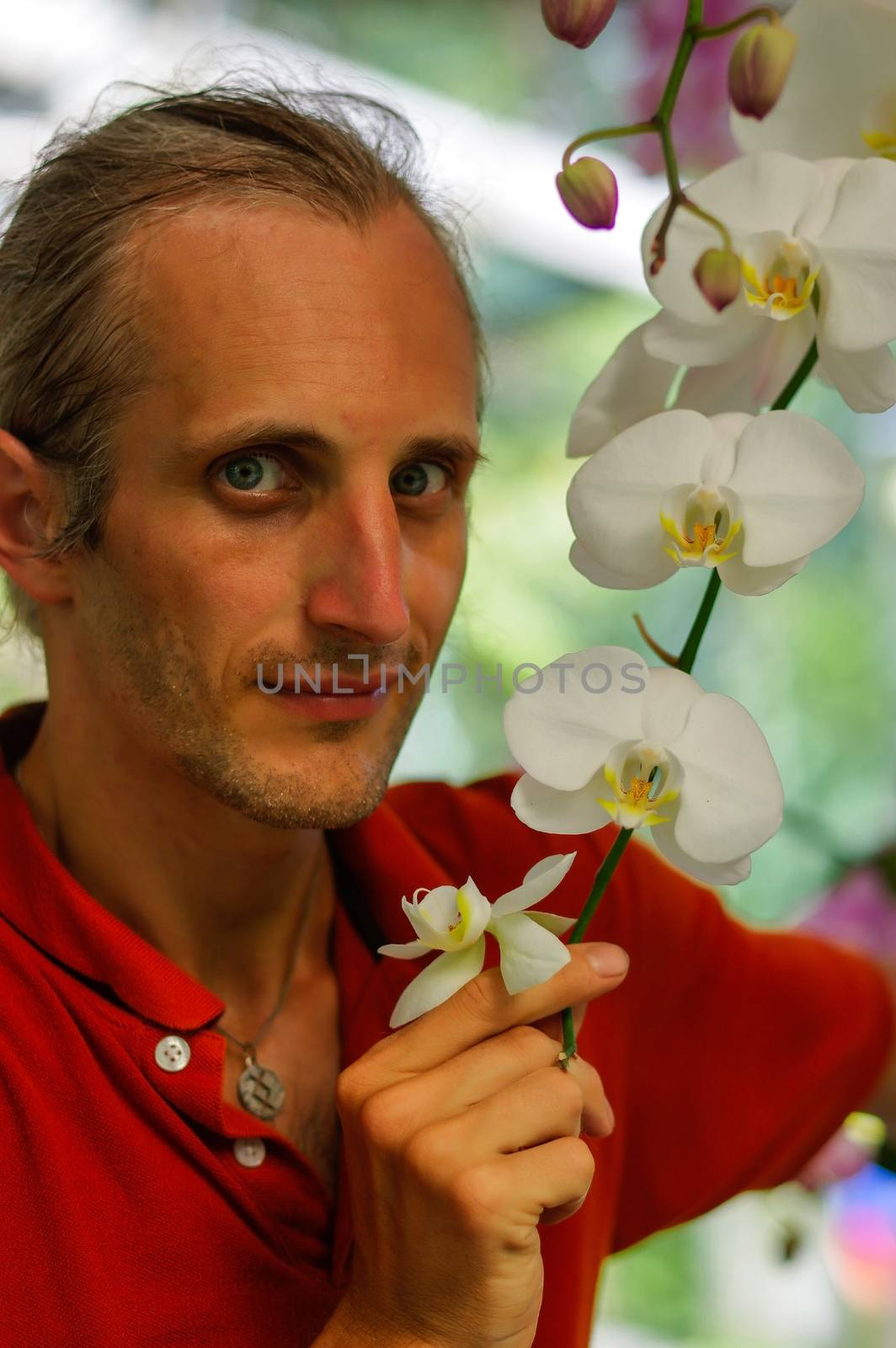 a handsome young man in garden smelling beautiful flowers in a sunny day by evolutionnow