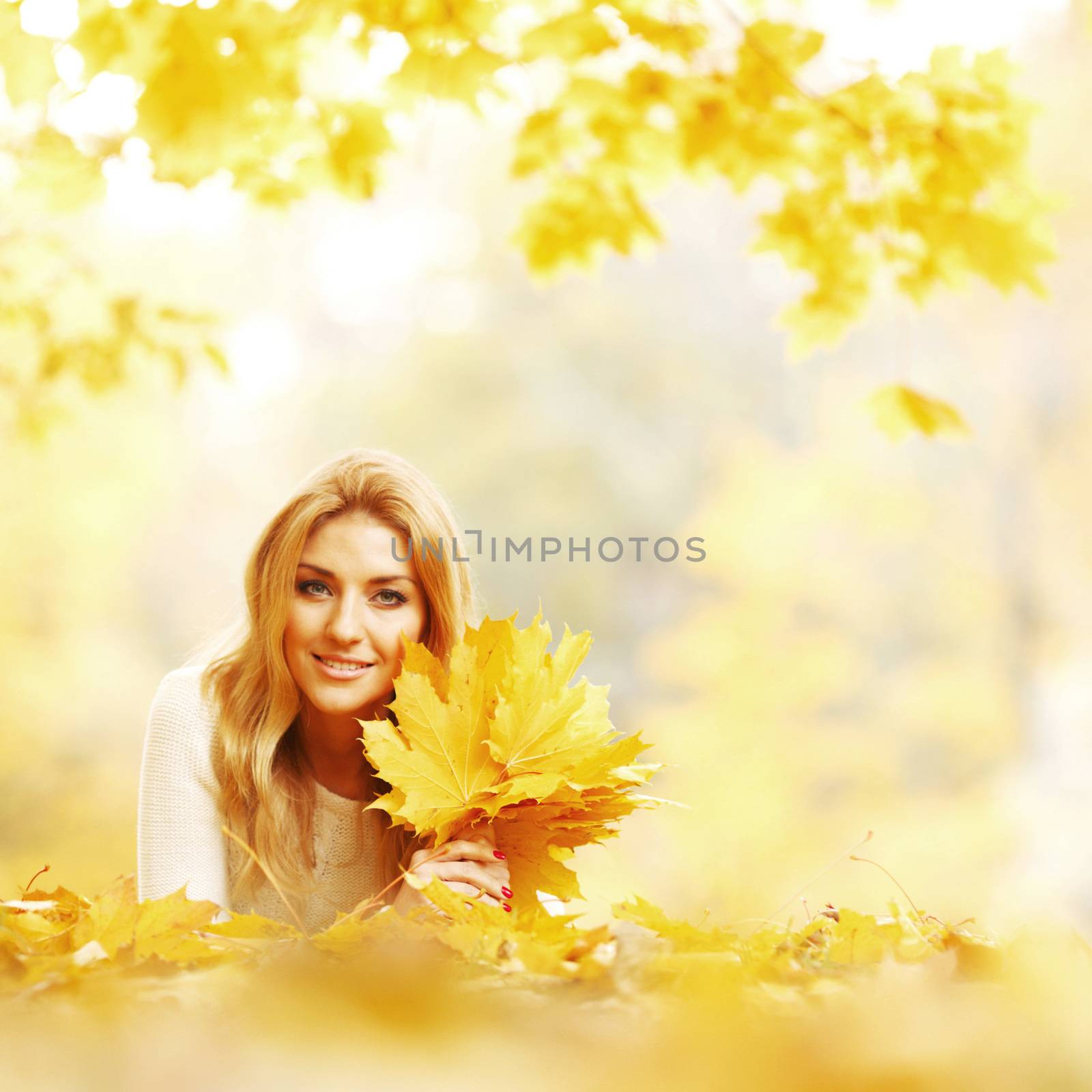 Young woman laying down on the ground covered dry autumnal foliage in beautiful park