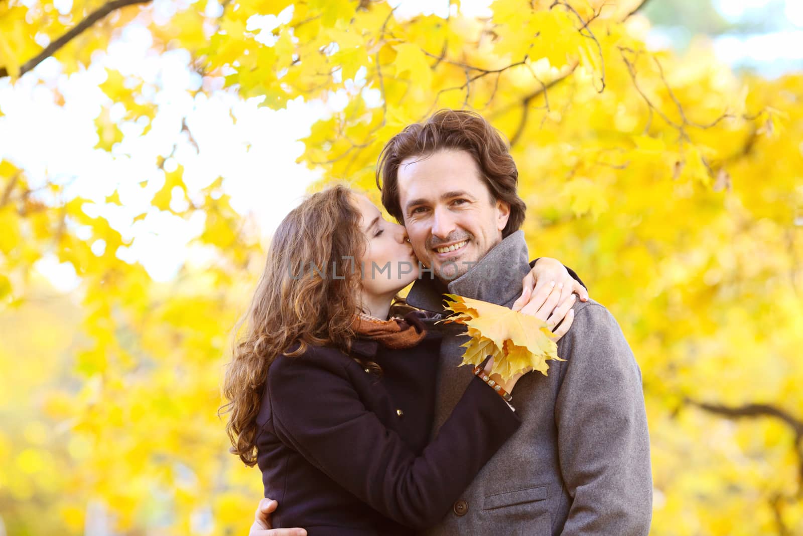 Happy couple kissing in autumn park with yellow trees