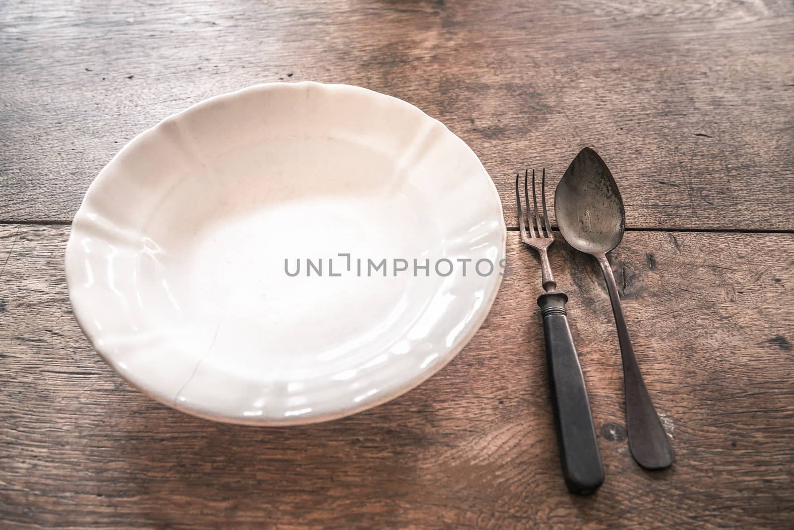 Retro image with an old fissured plate and rusty fork and spoon on a wooden table. Great as a frame or background with copy space.
