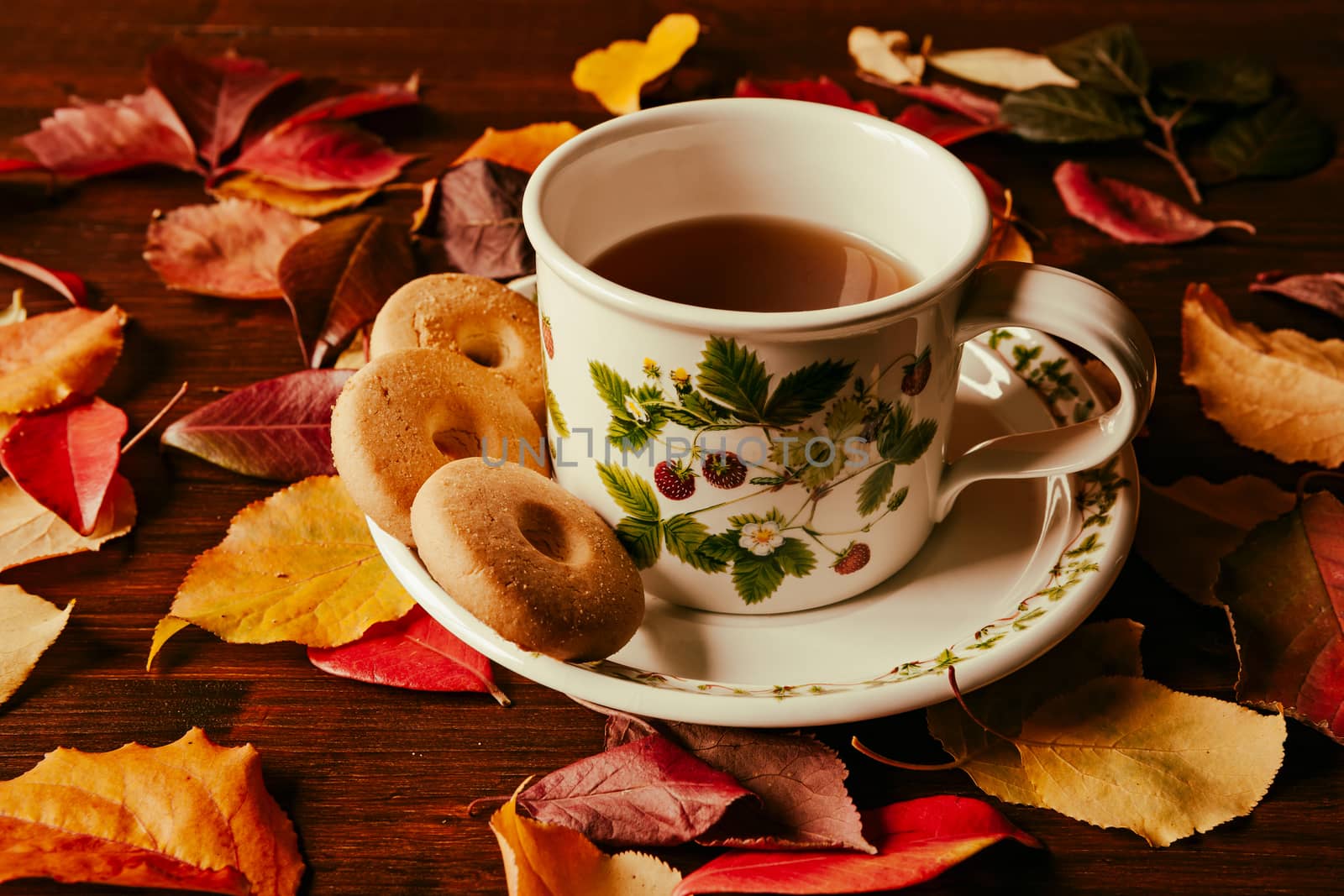 Cup of tea with biscuits and autumnal foliage over a dark table