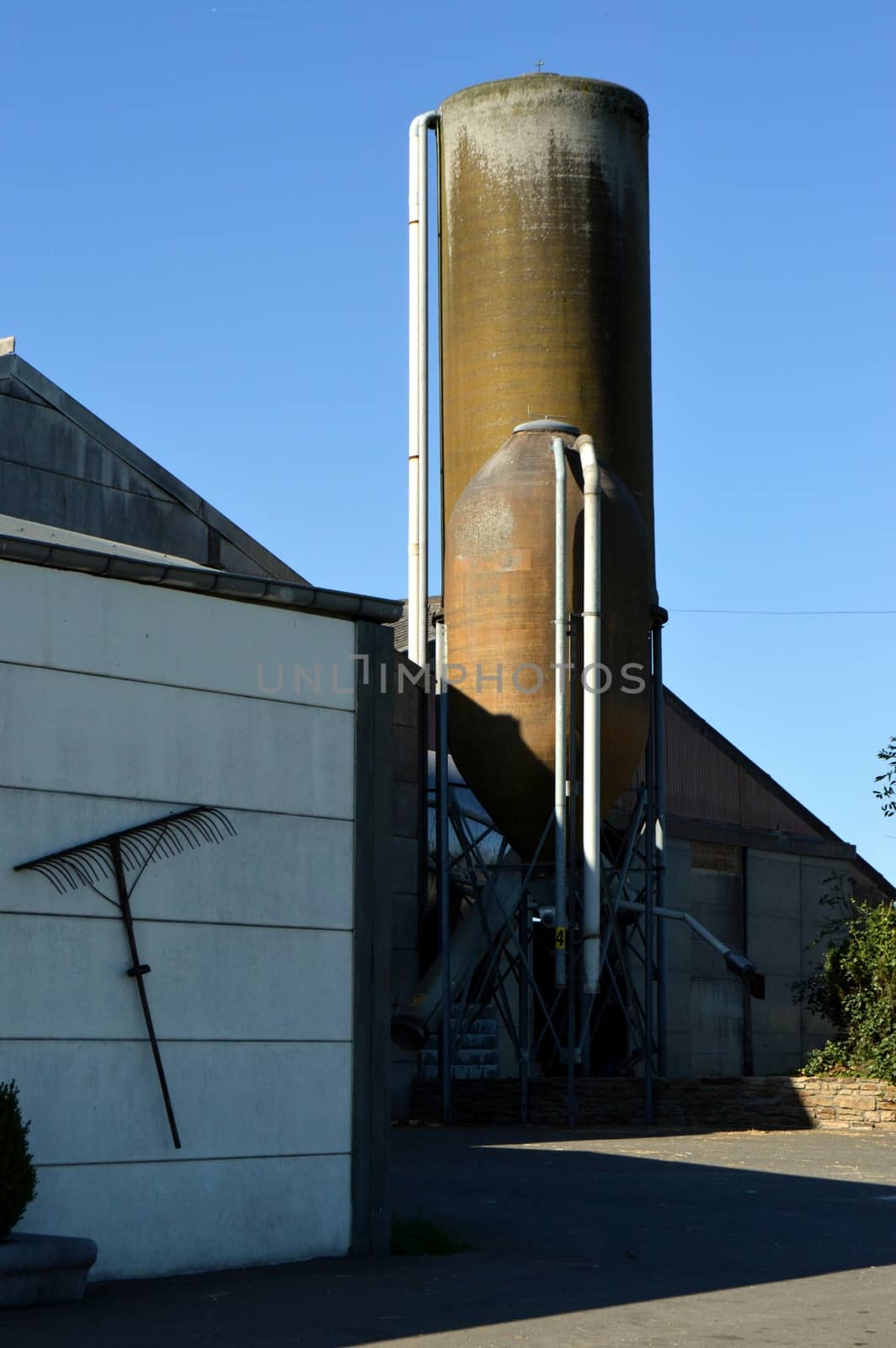 Grain silos in front of a barn with a blue sky.