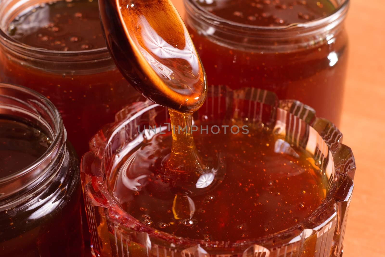 honey dripping from spoon, jars filled with honey, wooden table