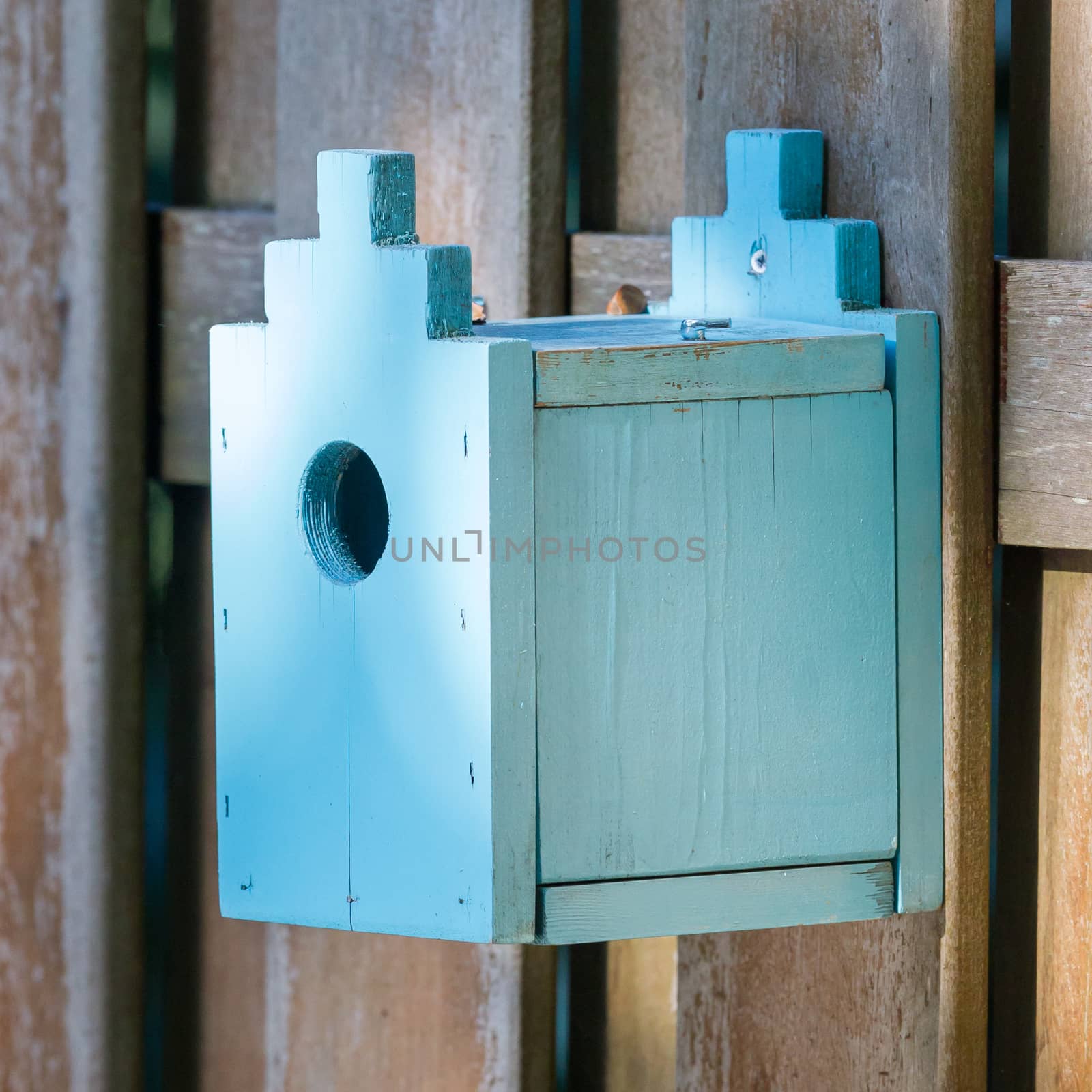 Blue birdhouse on a wooden fence in a garden
