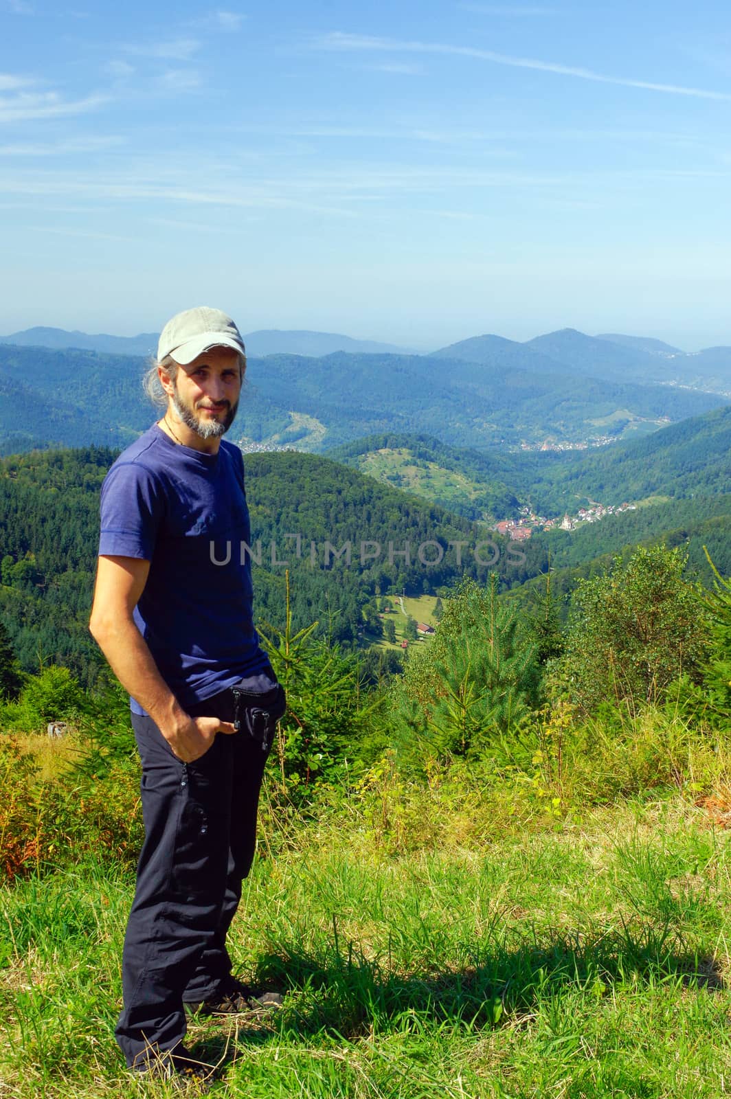 a bearded man, hiker with backpack, standing in the mountains and looks into the distance. Back view. Sunny day.