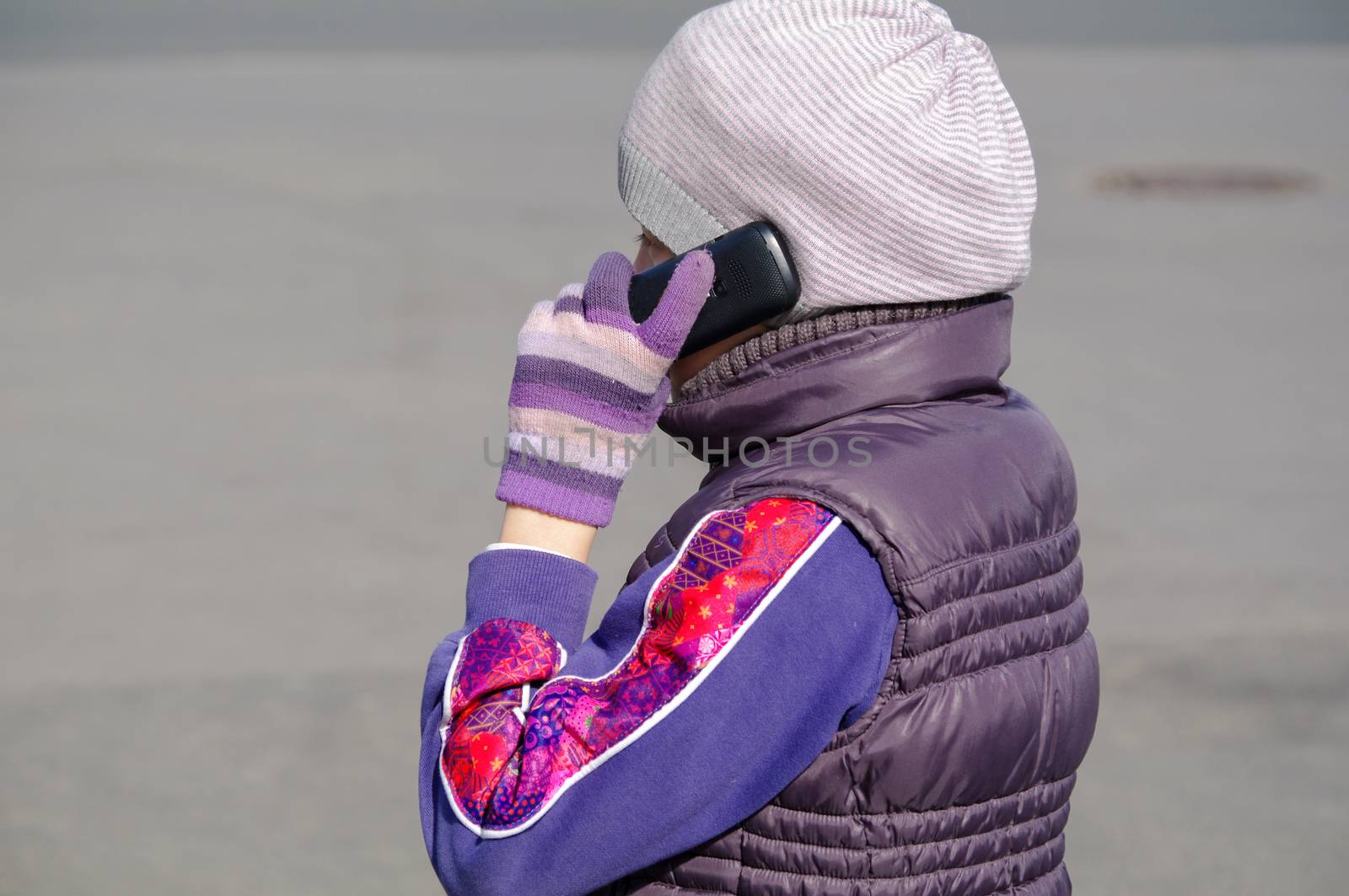 a Little girl speaks by mobile phone while standing outdoors.