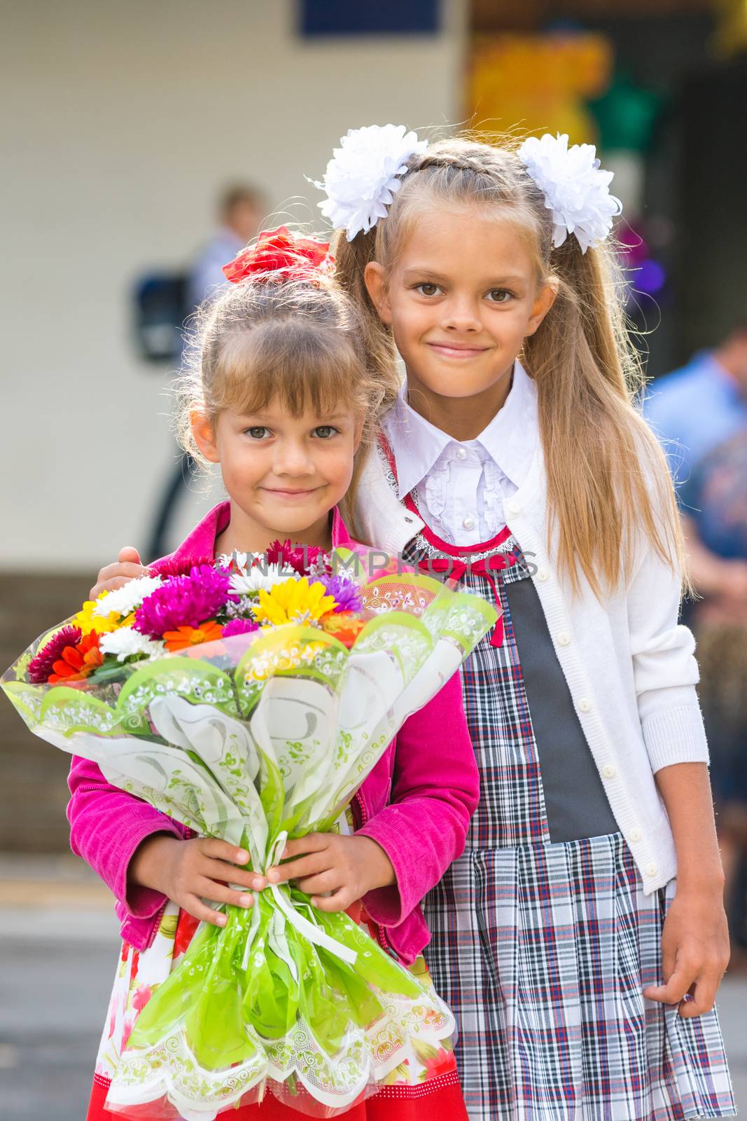 Portrait of two girls in school September 1 - the first-grader and her younger sister with a bouquet in hands