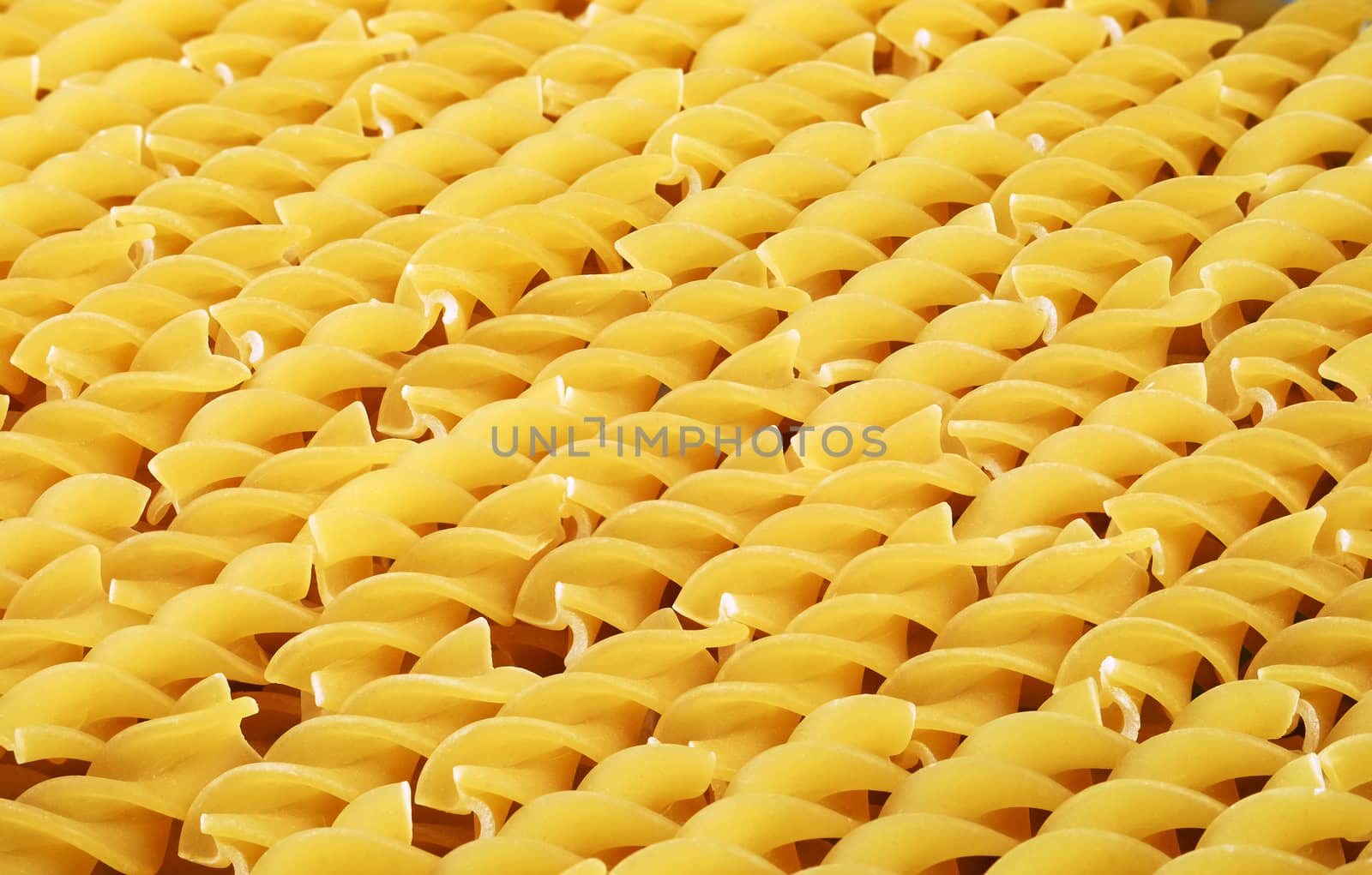Italian yellow short uncooked fusilli pasta closeup sorted diagonally for background or texture.