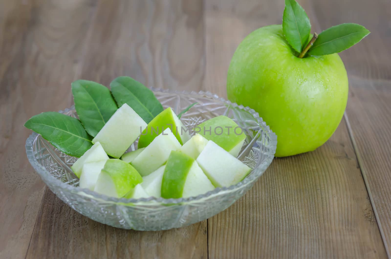 Ripe green apple with leaf and slice on a wooden background