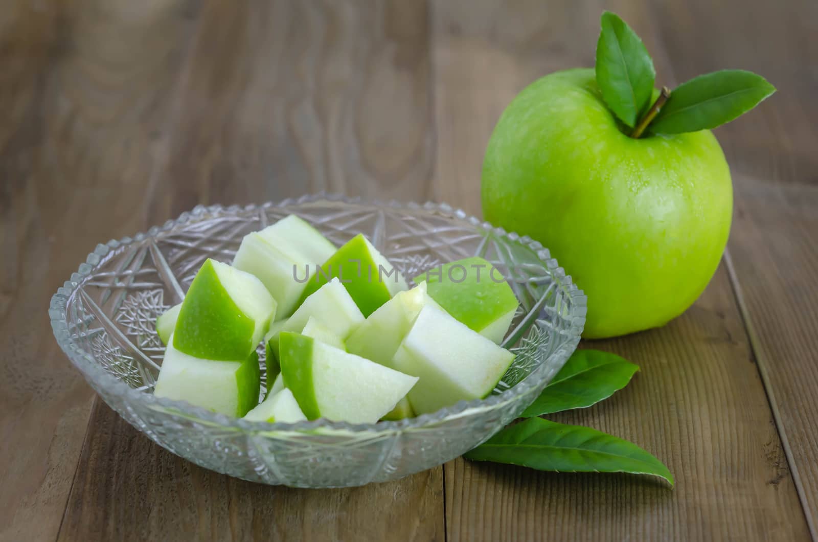 Ripe green apple with leaf and slice on a wooden background